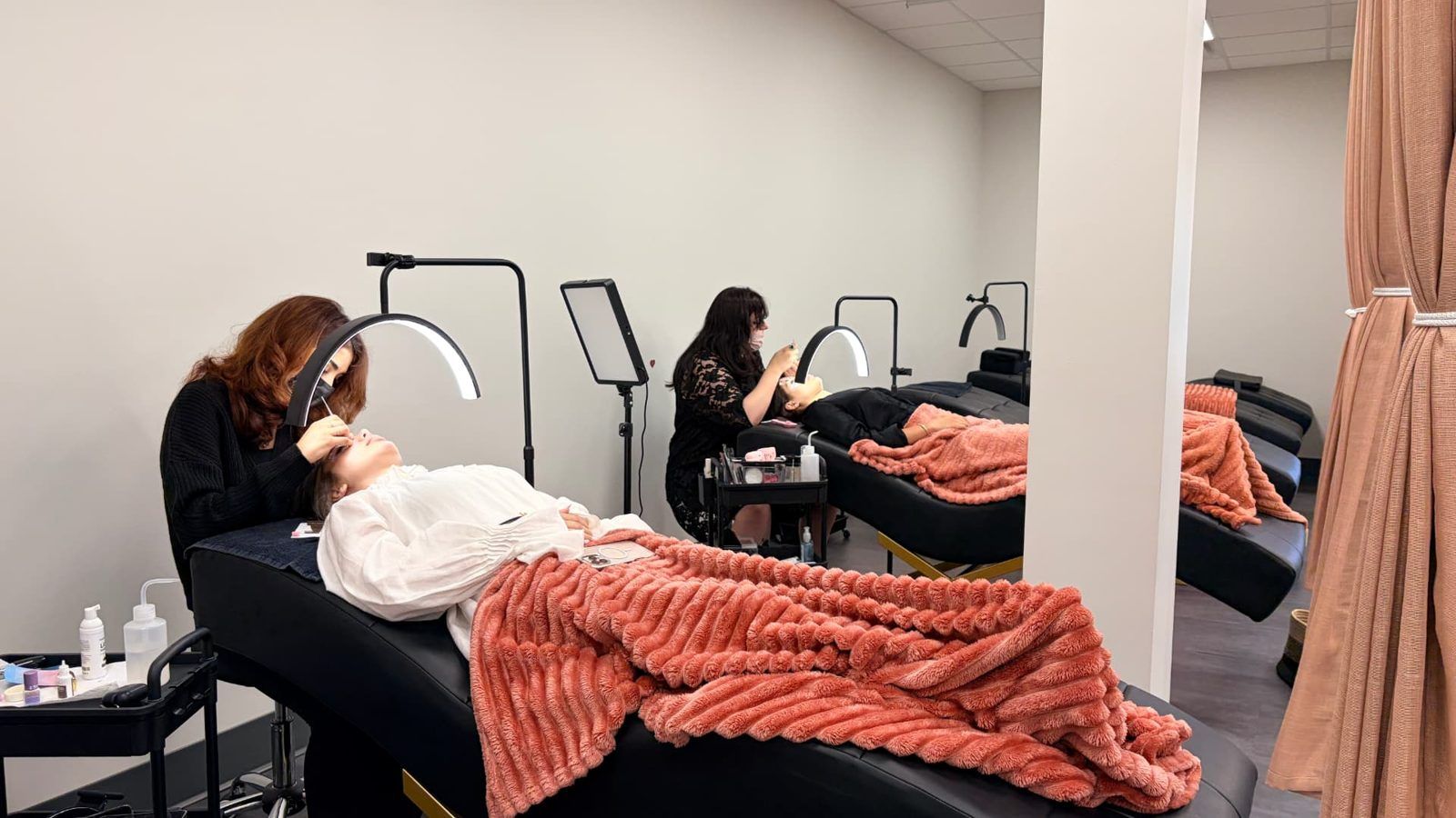 Two lash artists working with clients in the Lashh Aesthetics studio